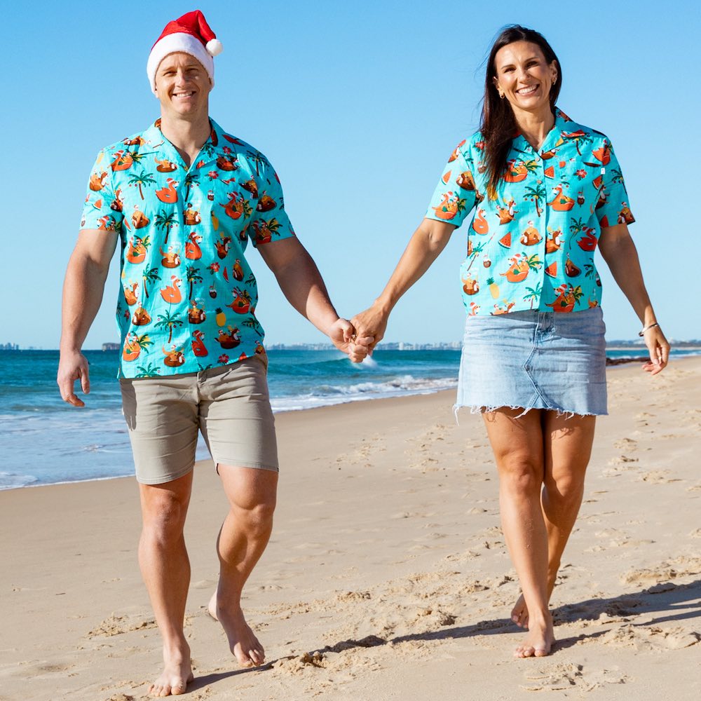 a man and a woman walking on a beach holding hands wearing Christmas shirts