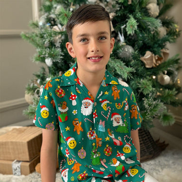 Boy wearing Holidaze Kids Unisex Festive Shirt with Christmas icons in front of a decorated tree. Ideal for boys & girls holiday outfits.