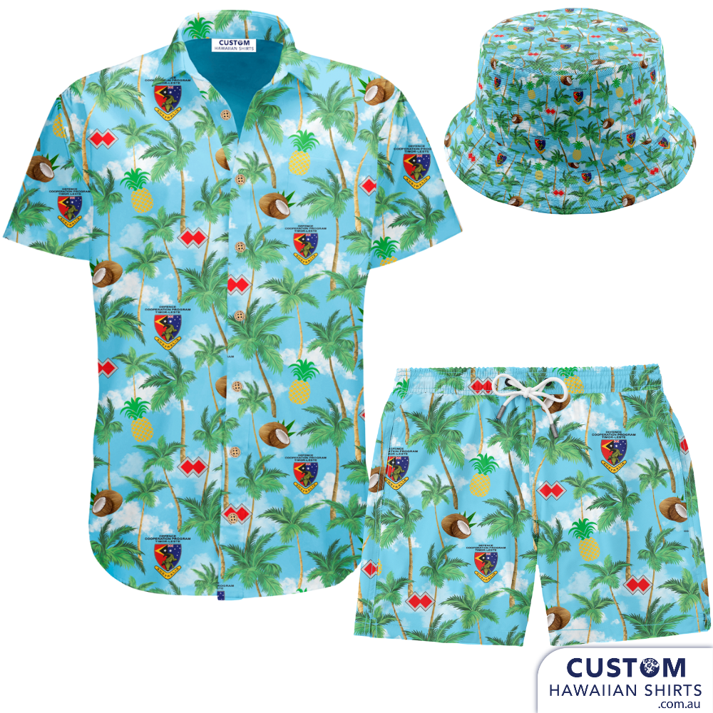 Defence Cooperation Program – Timor Leste  Showcasing some new Bucket Hats as well as custom shirts, shorts designed and despatched to Timor Leste to the ADF stationed there. The design features Palms, Pineapples, Coconuts and their logos on a sky blue background with clouds.  Mens Shirts Mens Shorts Bucket hats Embossed coconut buttons