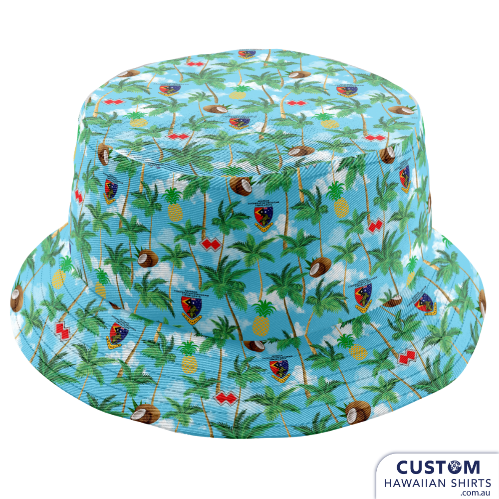 Defence Cooperation Program – Timor Leste  Showcasing some new custom shirts, shorts and bucket hats designed and despatched to Timor Leste to the ADF stationed there. The design features Palms, Pineapples, Coconuts and their logos on a sky blue background with clouds.  Mens Shirts Mens Shorts Bucket hats Embossed coconut buttons