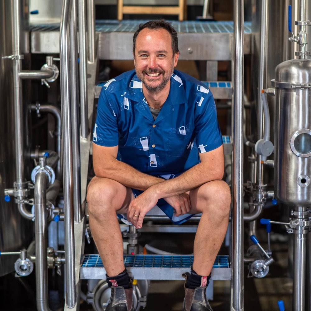 Man in a blue shirt sitting among industrial brewing equipment