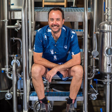 Man in a blue shirt sitting among industrial brewing equipment