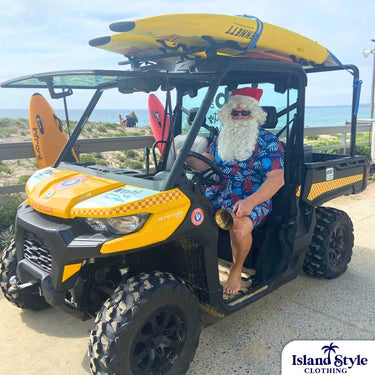 Santa wearing Wanda Surf Lifesaving Club custom shirt and shorts in navy with red and white leaf print, seated in a beach rescue ATV.