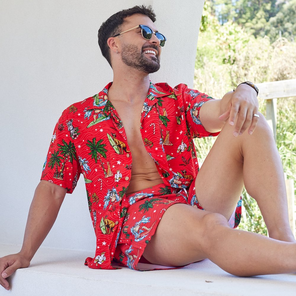 a man in a red Christmas shirt and shorts sitting on a porch