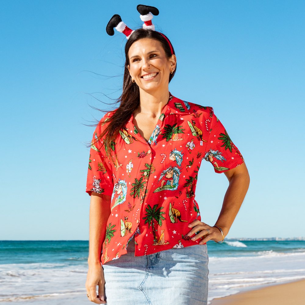 a woman standing on a beach wearing a red shirt and reindeer antlers on her