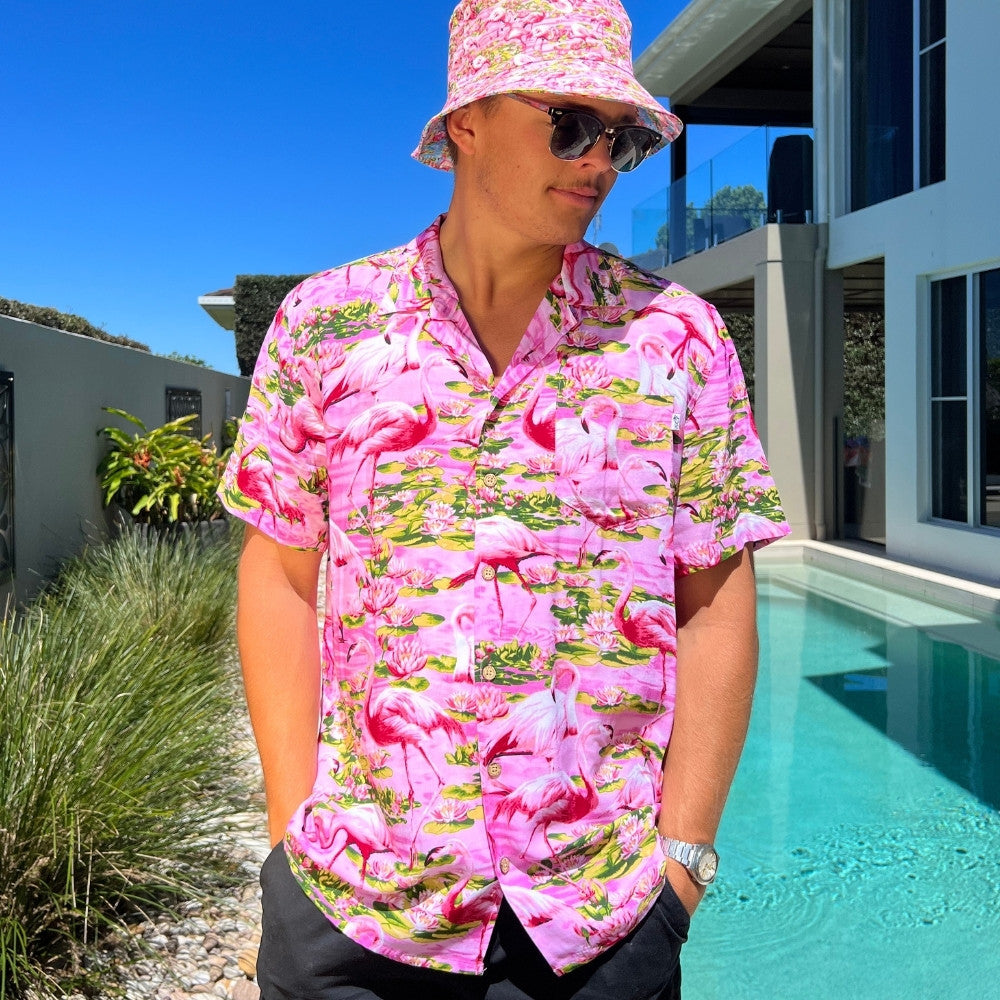 This classic men's Hawaiian shirt features vibrant pink flamingos printed on 100% rayon fabric. Complete with coconut buttons, it's perfect for a stylish yet comfortable island-style look. Steal the spotlight everywhere you go.