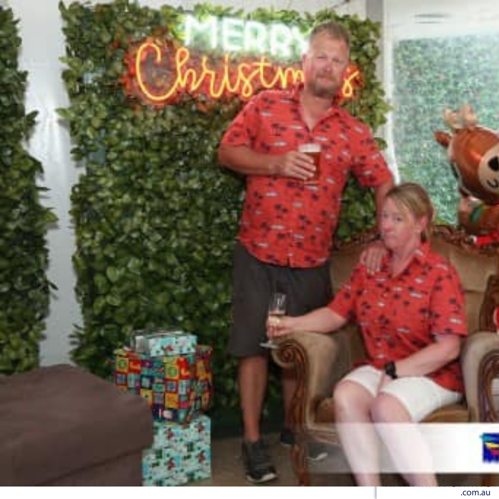 a man and a woman sitting on a couch in front of a christmas sign